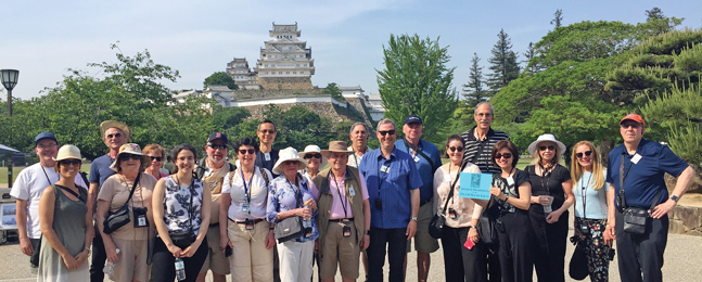 A line of people pose in front of an ancient castle in Japan